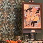 Art Deco-styled reception table with colorful floral centerpiece, elegant glassware, and vintage jazz musicians artwork on green wall