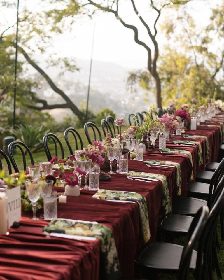 Long outdoor reception table with burgundy runners, pink blooms, and black chairs overlooking mountain vista