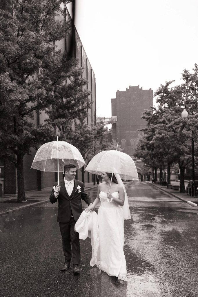 Bride and Groom walking in street with umbrellas during a rainy day captured by Films by Victoria.