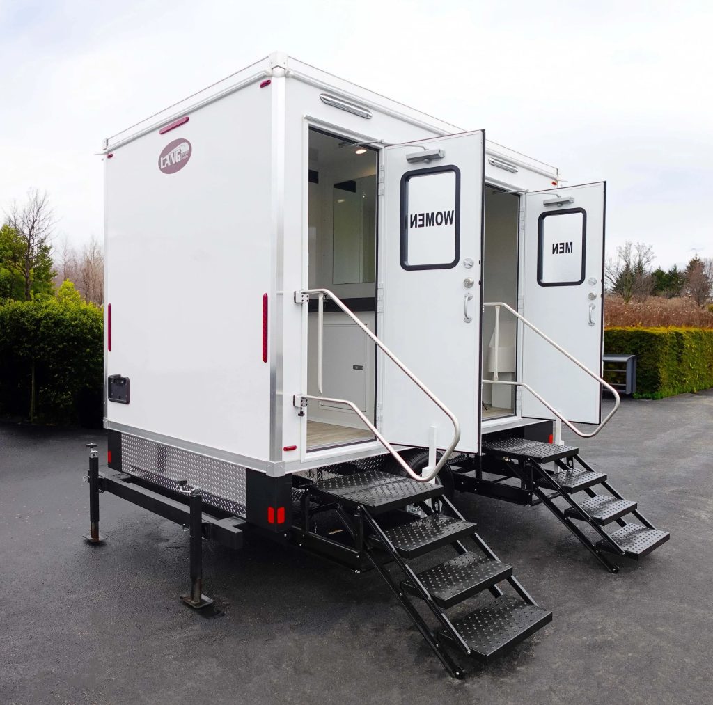 White portable restroom trailer with separate women's and men's entrances, featuring metal staircases with handrails