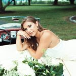 Bride reclining on vintage convertible adorned with white flowers and greenery