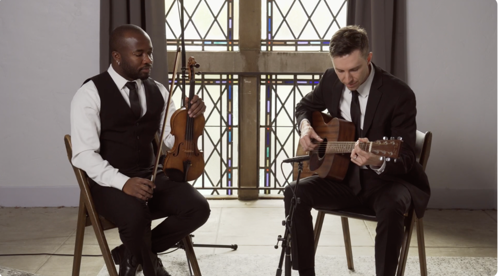 Two musicians in formal attire performing acoustic violin and guitar duo at elegant venue