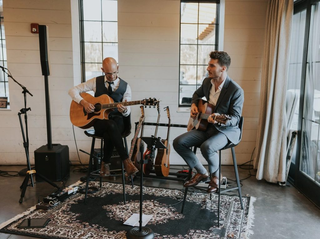 Two male musicians performing acoustic guitars at wedding reception in modern venue with large windows