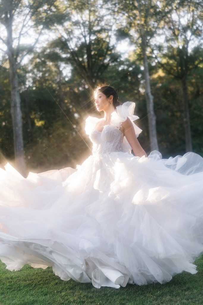 Bride in dramatic tulle ball gown with puff sleeves and flowing skirt photographed at sunset in wooded setting