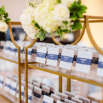Gold bar cart with escort cards and white floral arrangements at wedding reception