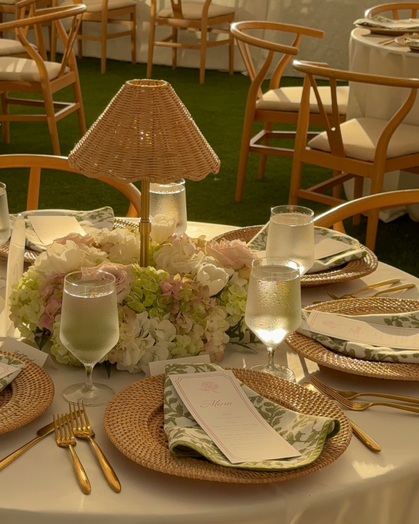 Wedding reception table detail featuring wicker lamp, hydrangea centerpiece, and gold place settings