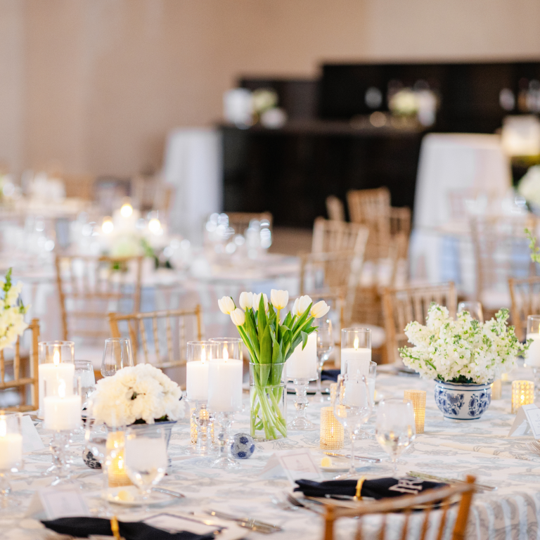 Elegant wedding reception table with white tulips, pillar candles, and blue chinoiserie vases featuring gold chiavari chairs