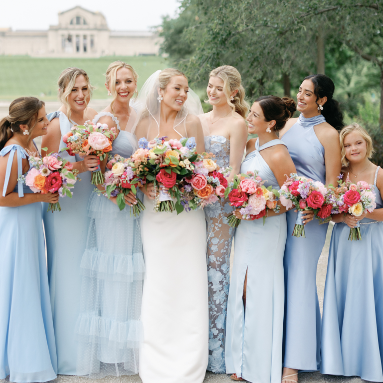 Bride and bridesmaids in coordinating blue dresses holding vibrant floral bouquets outdoors