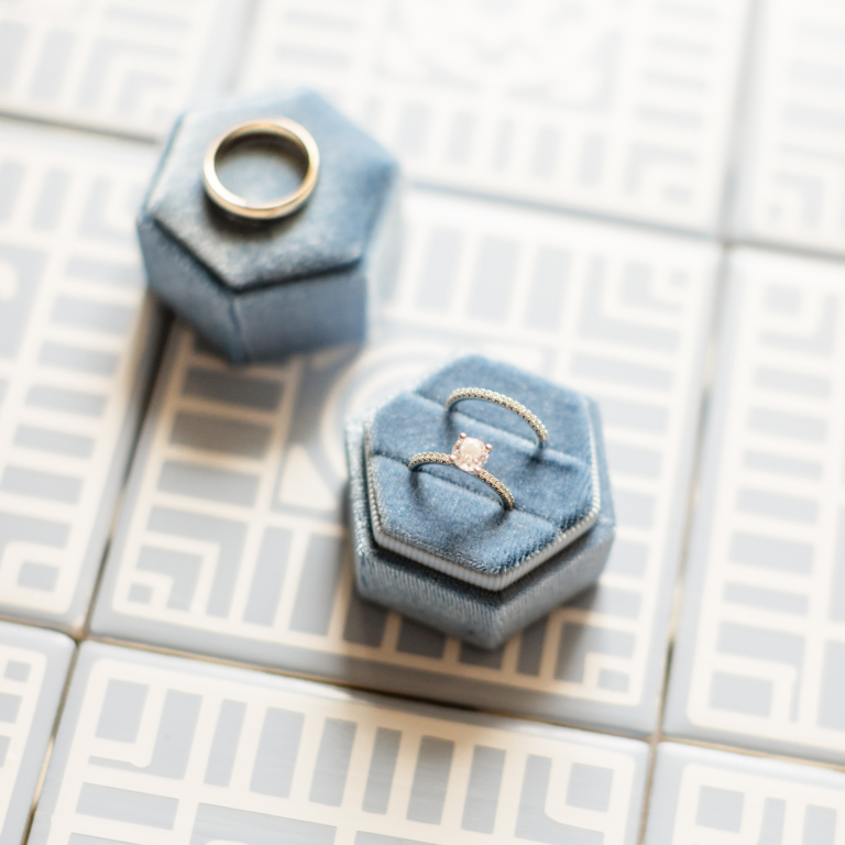Wedding rings displayed in dusty blue velvet hexagonal boxes on geometric patterned tile