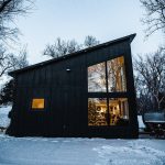 Modern black barn-style venue illuminated at dusk in winter snow