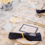 Elegant place setting with navy napkin, scalloped menu card, gold flatware, and patterned tablecloth
