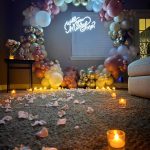 Romantic marriage proposal setup with pastel balloon arch, "Will you Marry Me?" neon sign, rose petals, and candles