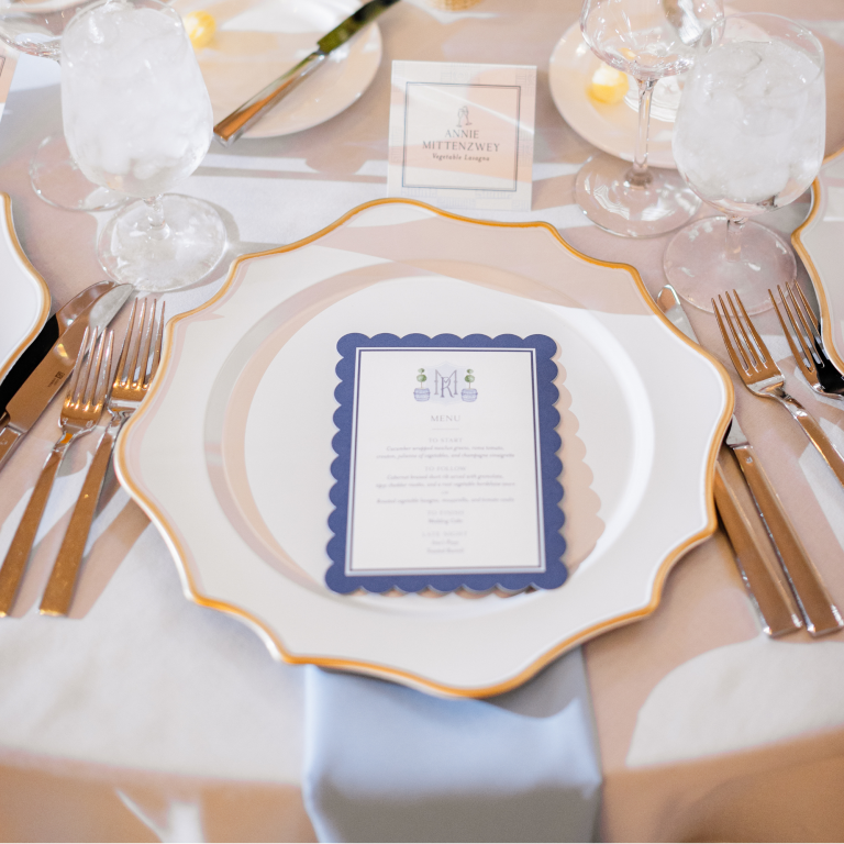 Formal place setting with scalloped gold-rimmed plates, blue-bordered menu card, and crystal glassware