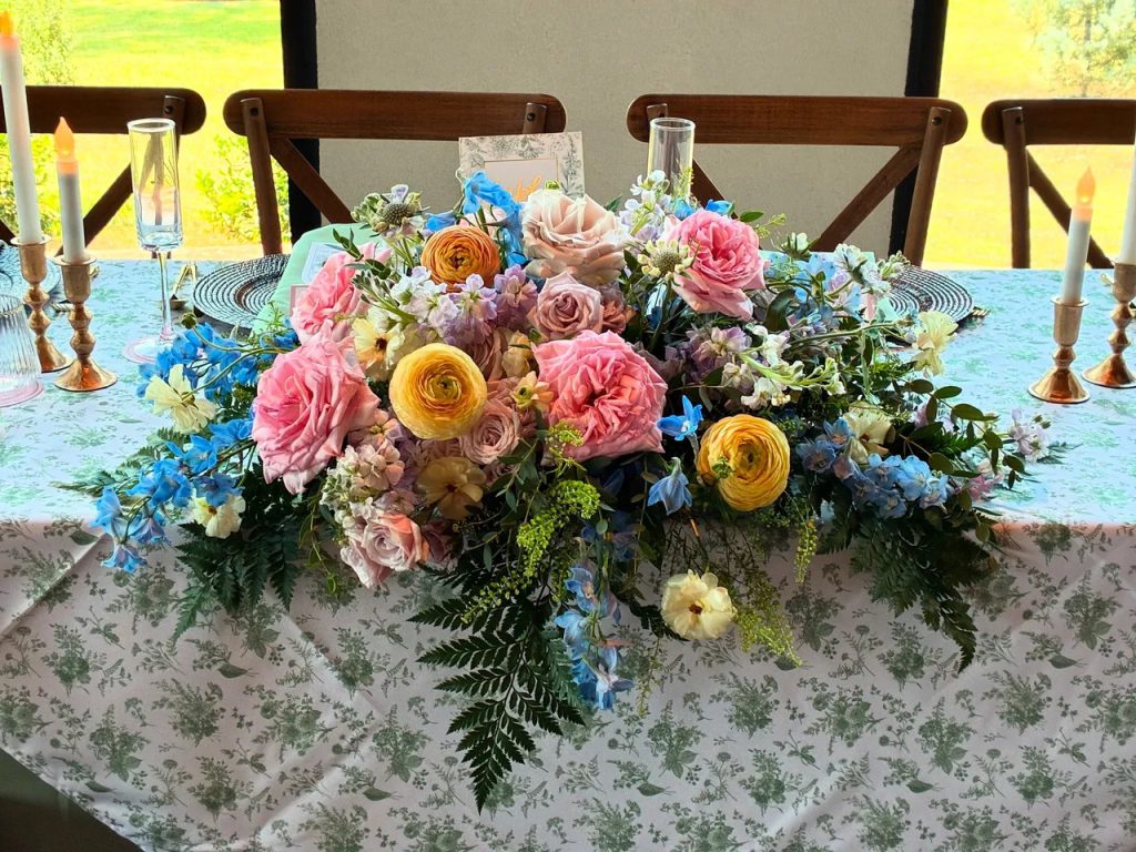 Colorful floral arrangement with pink, yellow, and blue blooms on lace table runner