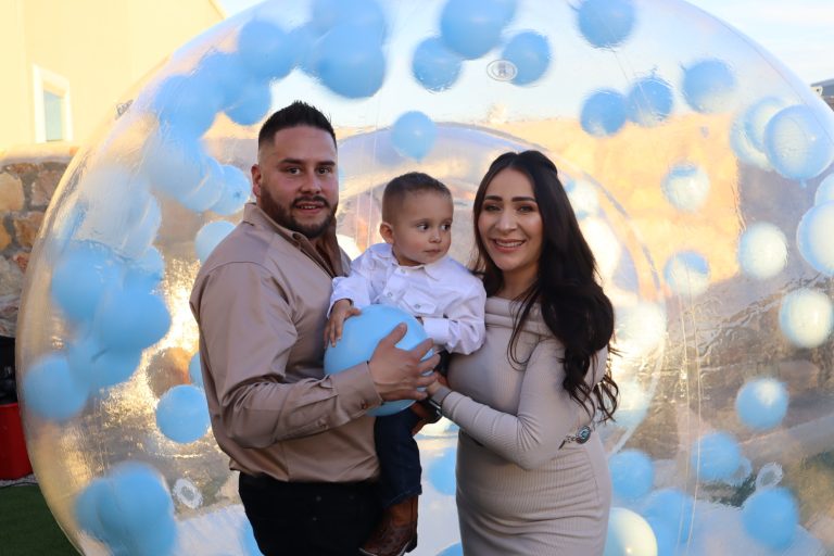 Family of three posing beneath blue and white balloon arch