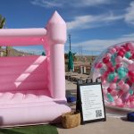 Pink castle bounce house and circular balloon installation at outdoor event venue