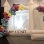 White bounce house with colorful balloon arch and "Shake It Off" event backdrop