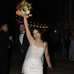 Bride in white gown raising her colorful bouquet in celebration