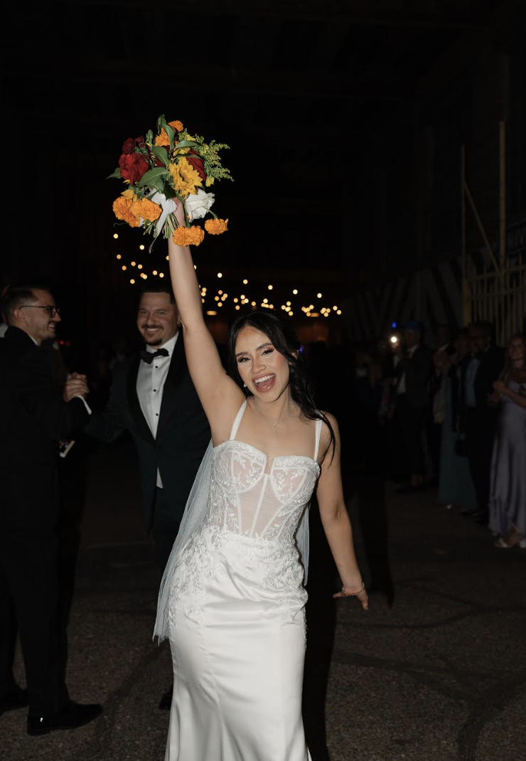 Bride in white gown raising her colorful bouquet in celebration