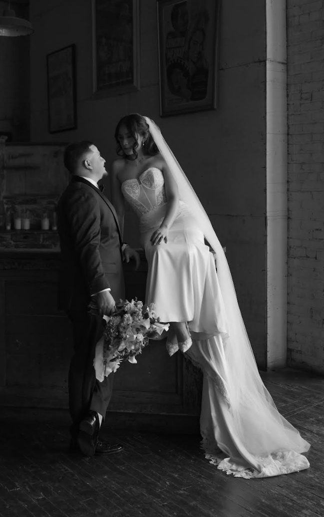 Black and white portrait of bride in lace sweetheart gown with flowing train and groom in industrial loft