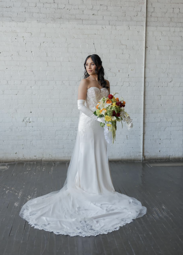Bride in strapless lace gown with cathedral train holding vibrant yellow, orange, and burgundy cascading bouquet