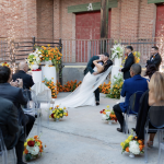 Wedding party gathered outside brick church entrance with floral arrangements