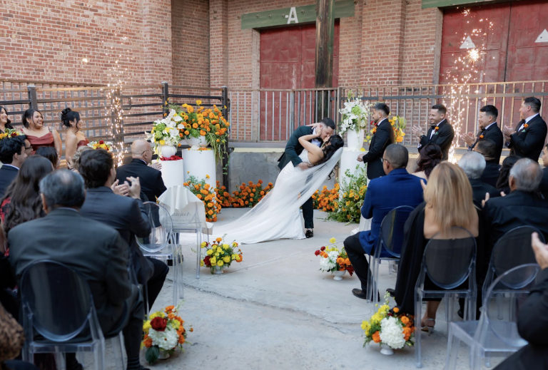Wedding party gathered outside brick church entrance with floral arrangements