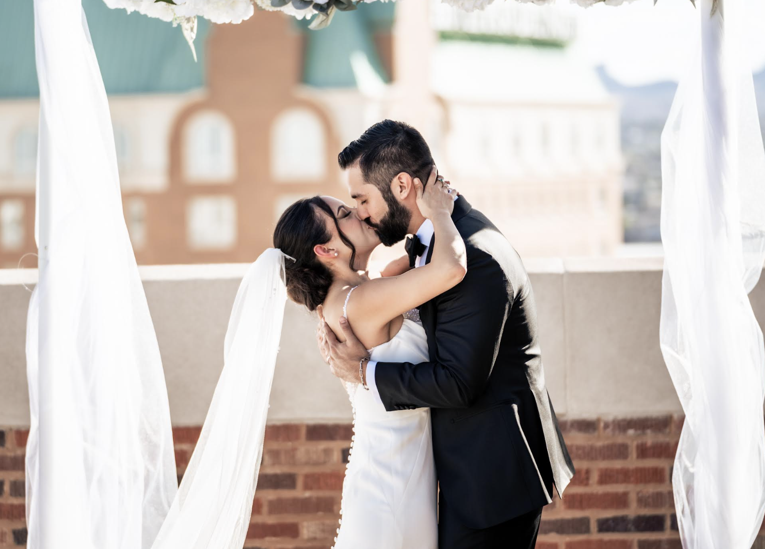 Couple embraces near large "W" letter against brick building backdrop