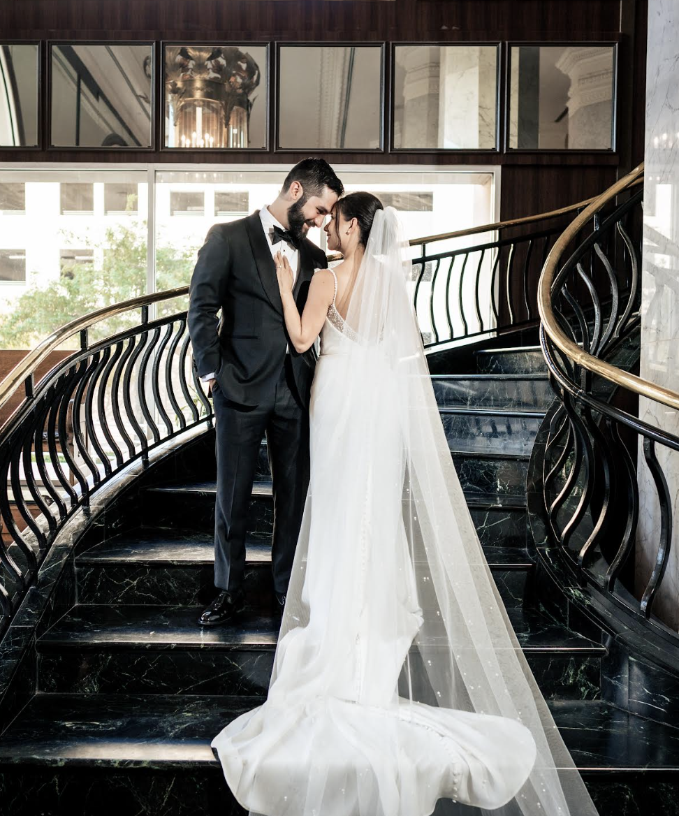 Close-up of newlyweds kissing on grand staircase with flowing bridal veil