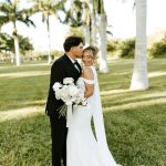 Newlyweds embrace under palm trees in Miami, bride holding white and blush bouquet