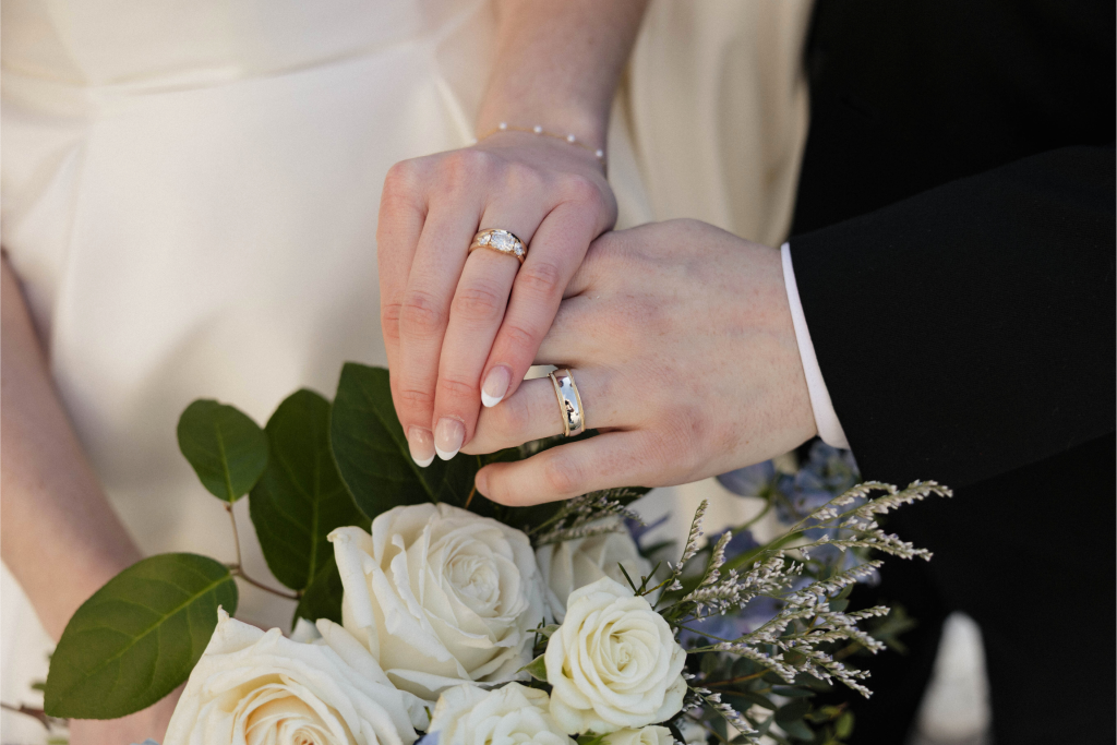 Newlyweds' hands with wedding rings resting on white rose bouquet