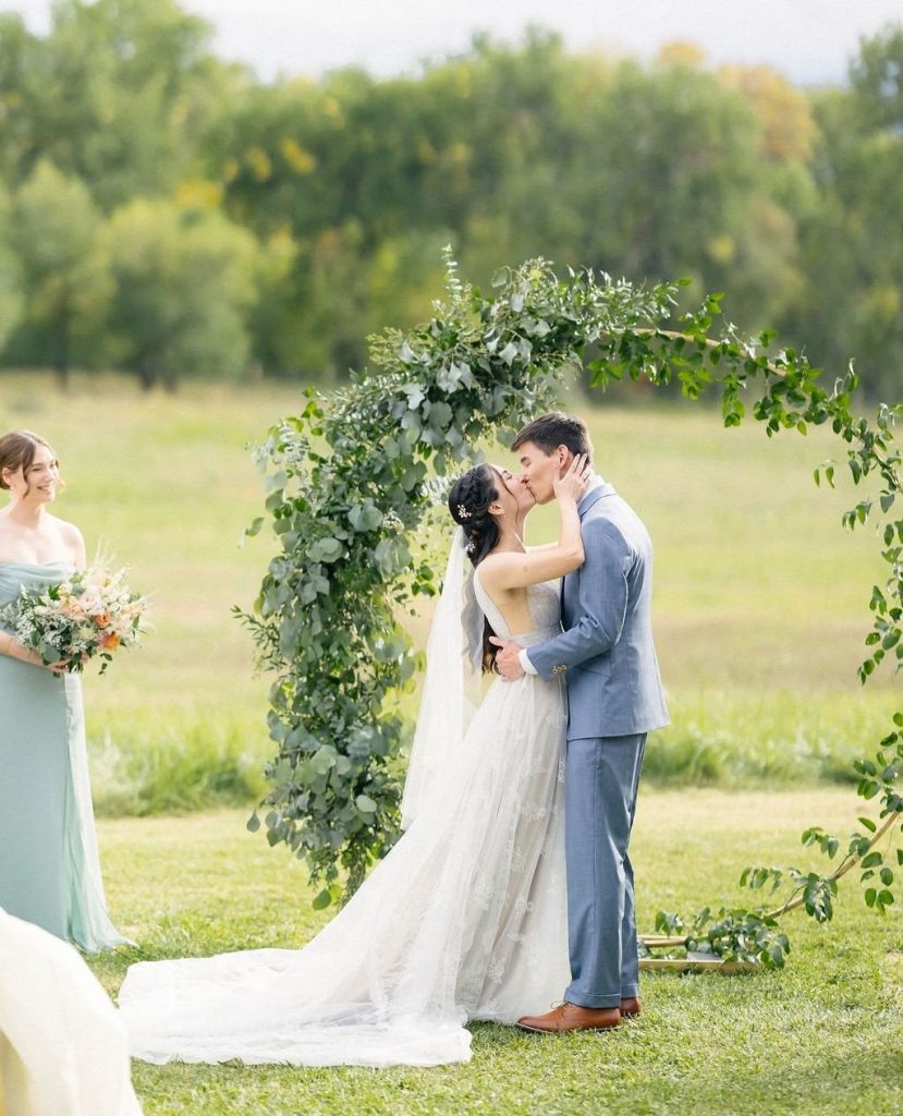 Brittany and Joshua share their first kiss beneath a lush greenery arch at their outdoor Colorado ceremony