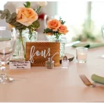 Wedding reception table centerpiece with peach roses in glass vases and wooden table number four sign