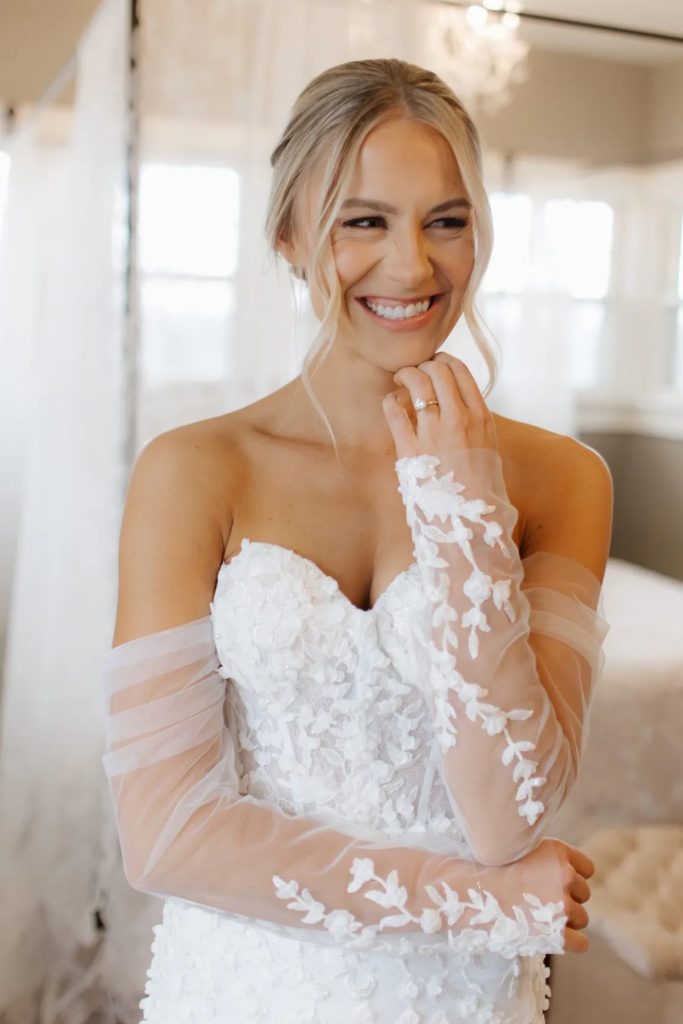Smiling bride in lace wedding dress with floral appliqué sleeves and elegant updo