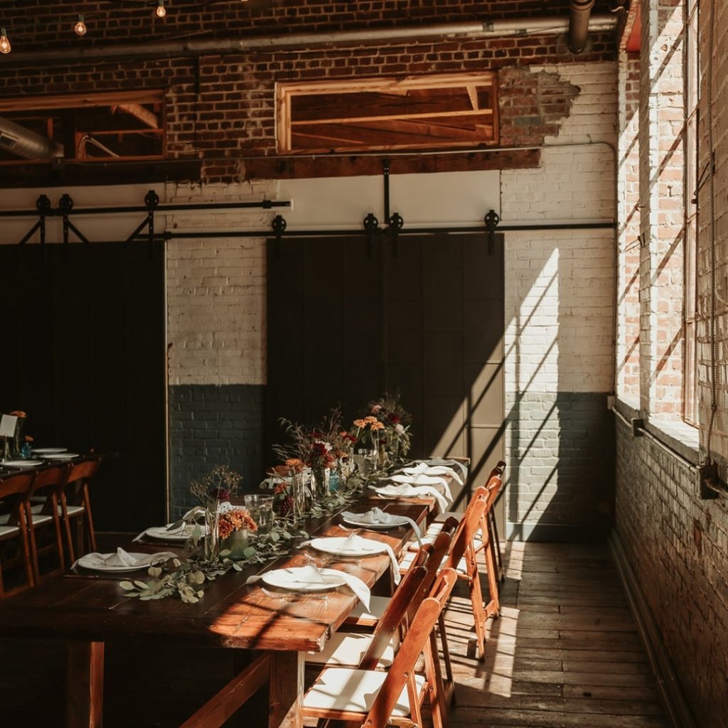 Rustic industrial wedding reception table with Edison lights and exposed brick at Forest Hall at Chatham Mills