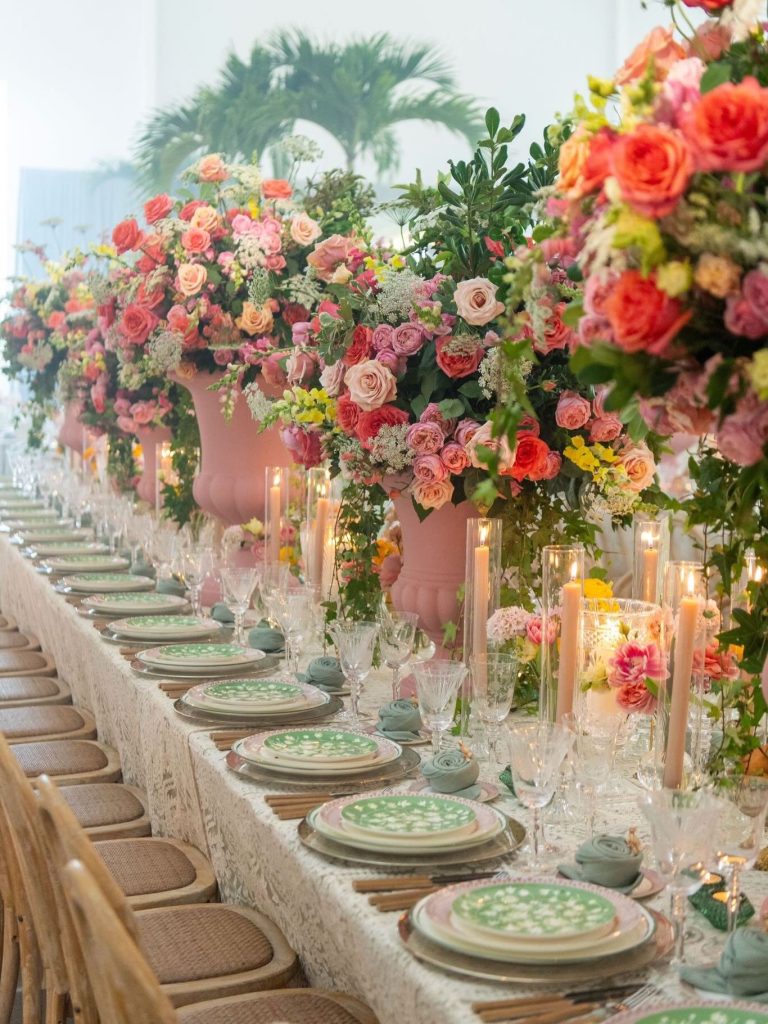 Long reception table with coral and pink floral centerpieces, green china, and elegant place settings