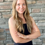 Madeline, Active Wellness fitness trainer in black workout attire with arms crossed against stone wall