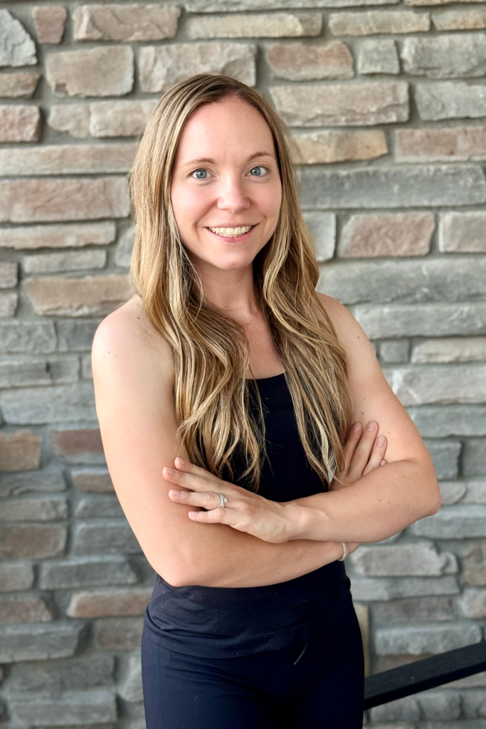 Madeline, Active Wellness fitness trainer in black workout attire with arms crossed against stone wall