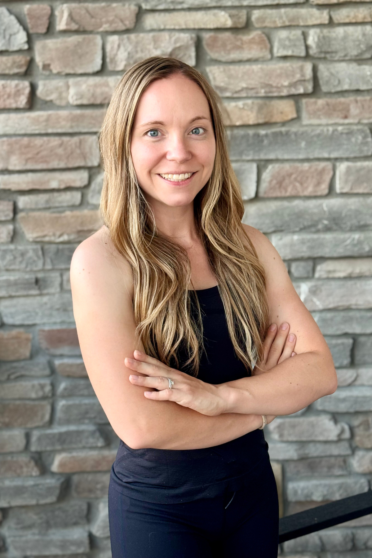 Madeline, Active Wellness fitness trainer in black workout attire with arms crossed against stone wall