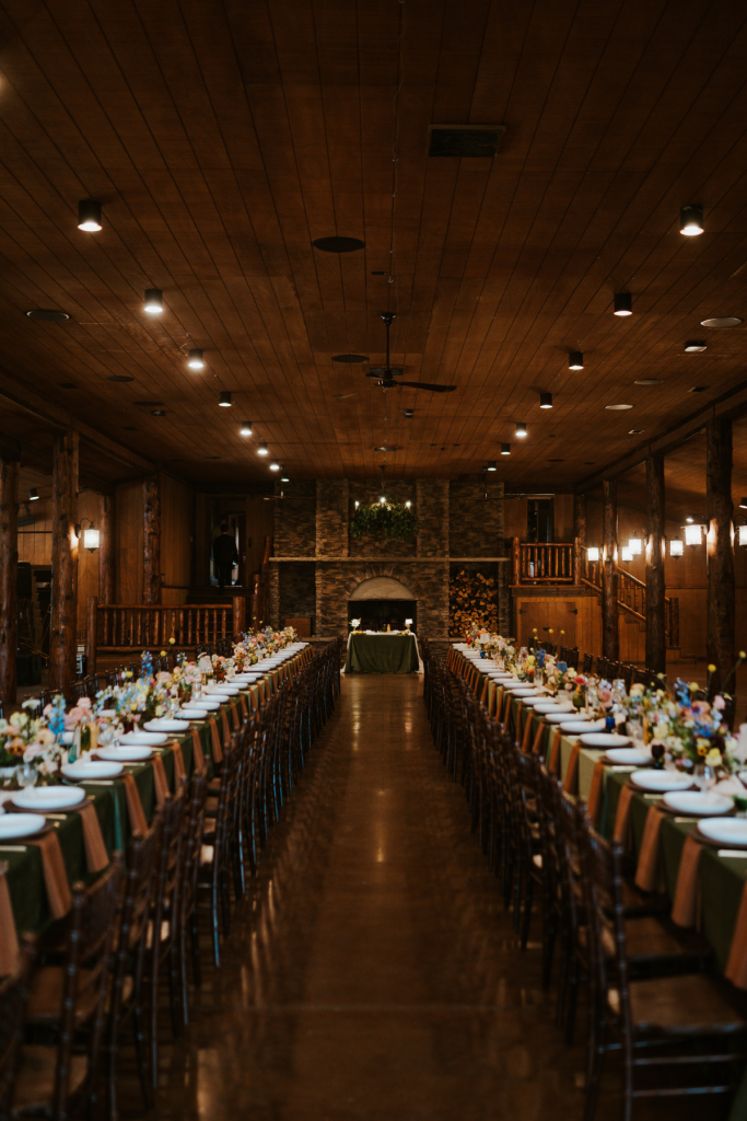 Rustic lodge reception hall with long banquet tables, green napkins, and stone fireplace at Spruce Mountain Ranch