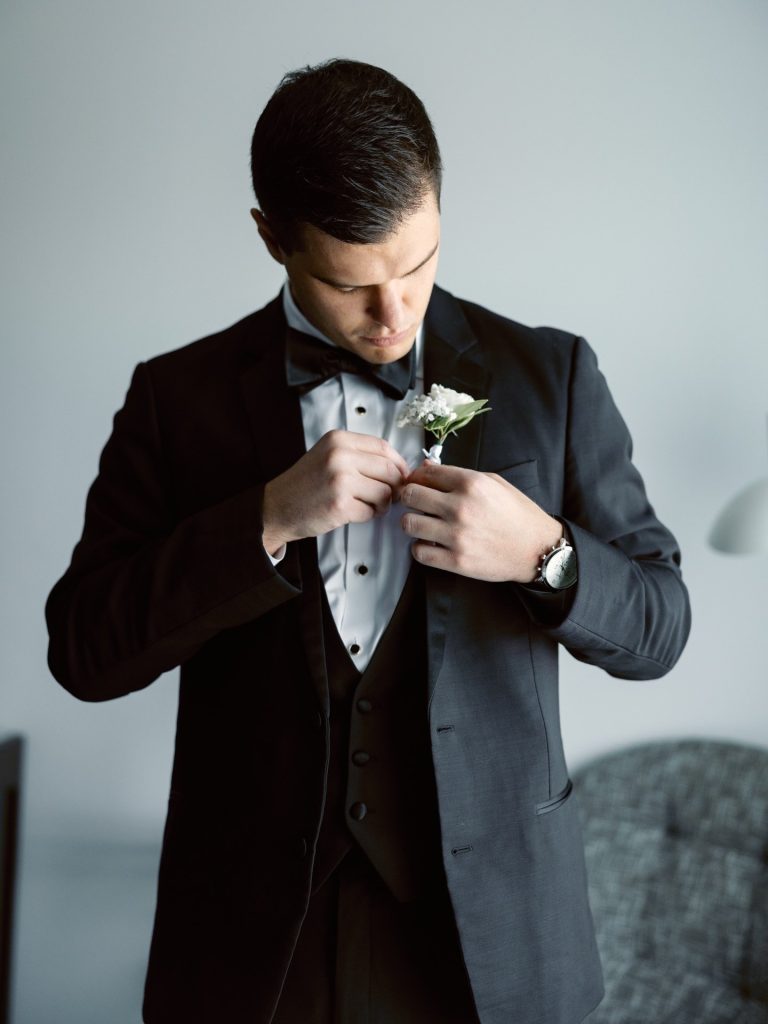 Steve fastening white boutonniere to his black tuxedo with bow tie
