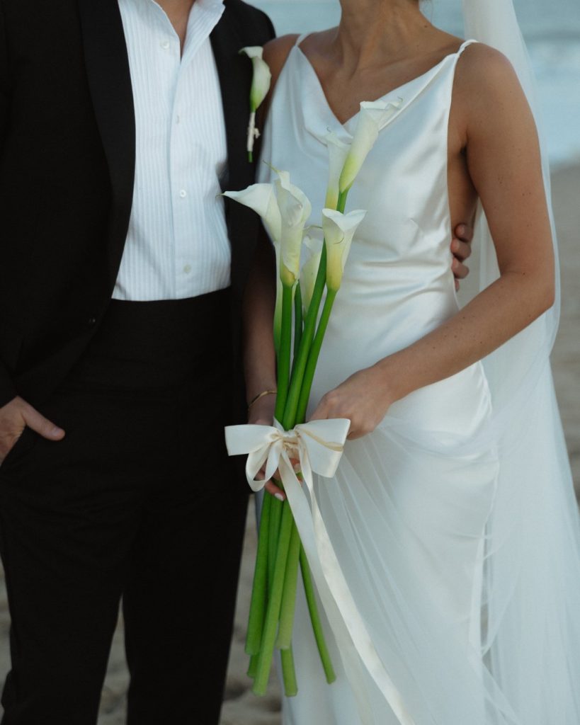 Bride holding calla lily bouquet beside groom during sunset portraits at coastal micro wedding at Addy Sea in Bethany Beach, Delaware.
