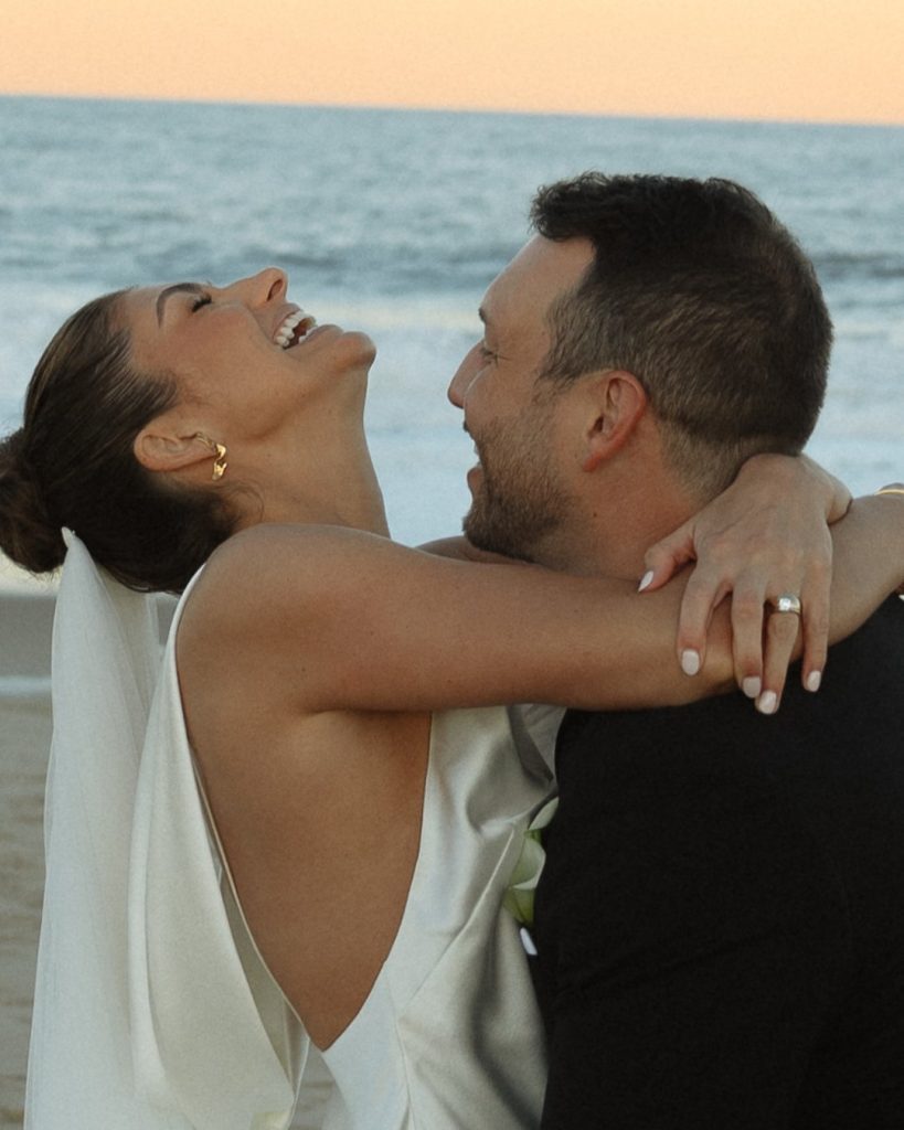 Bride and groom embracing on beach at golden hour with ocean backdrop at intimate Addy Sea wedding in Bethany Beach, Delaware.