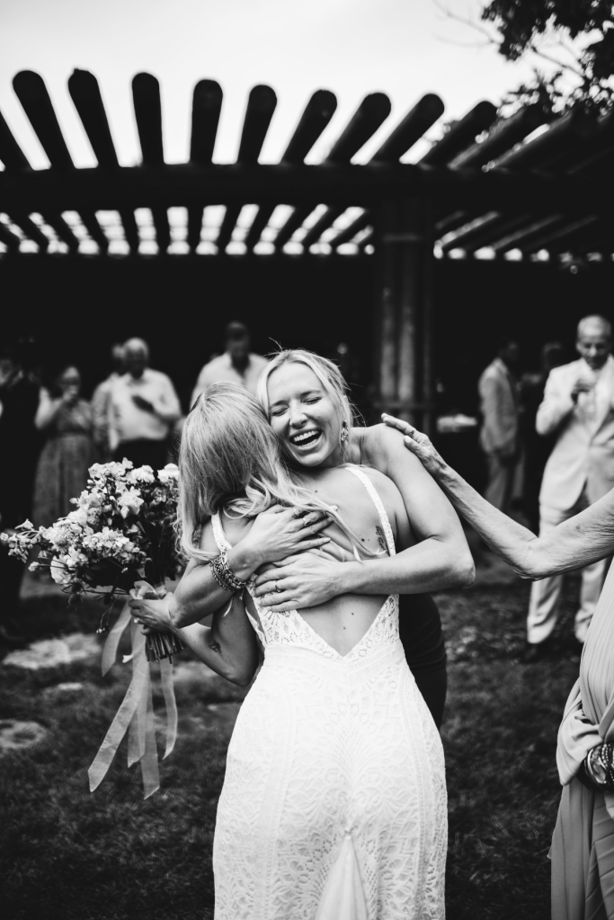 Mallory embraces a guest while holding her wildflower bouquet during the outdoor ceremony at Spruce Mountain Ranch