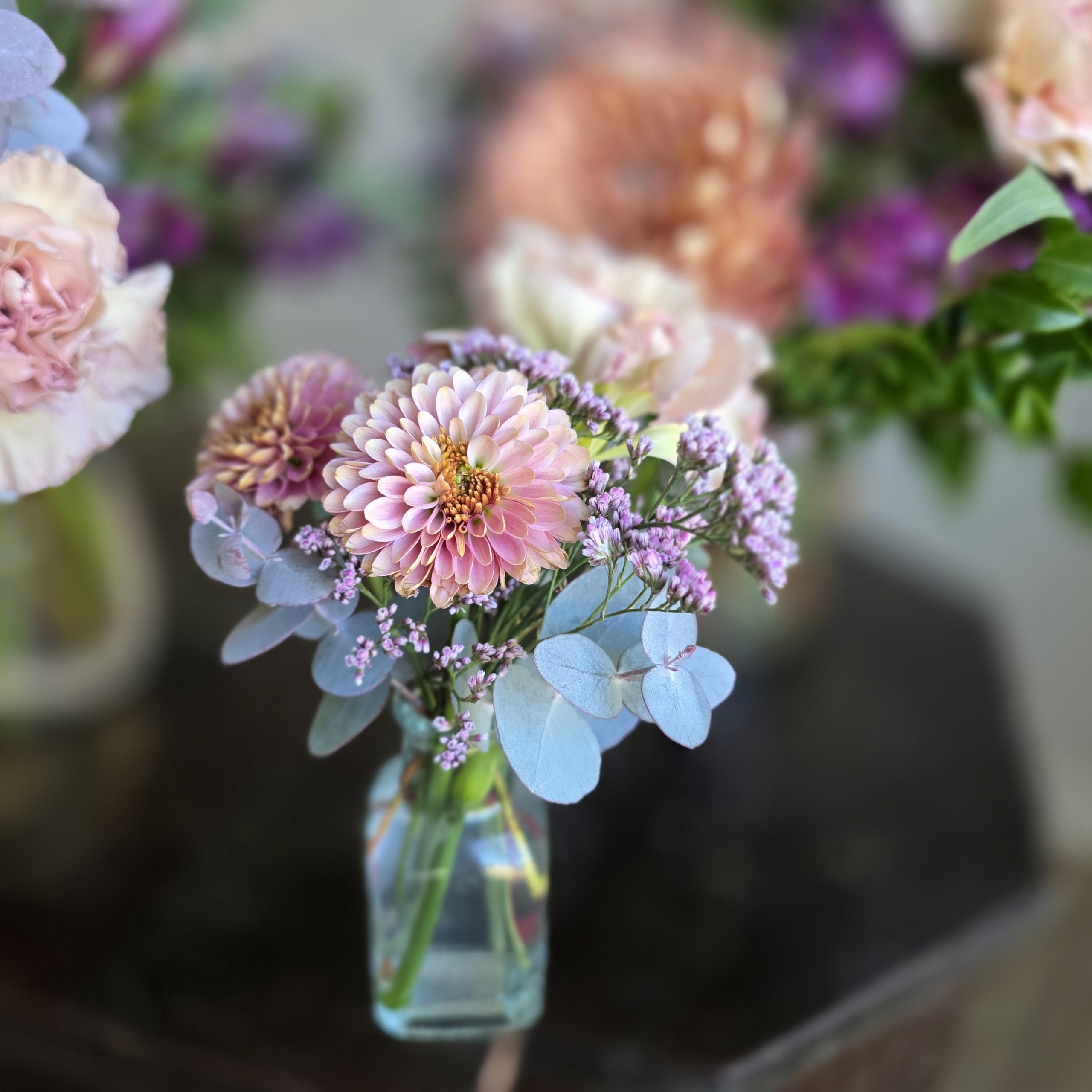 Wedding bouquet featuring dahlias, purple statice, and eucalyptus in clear glass bottle