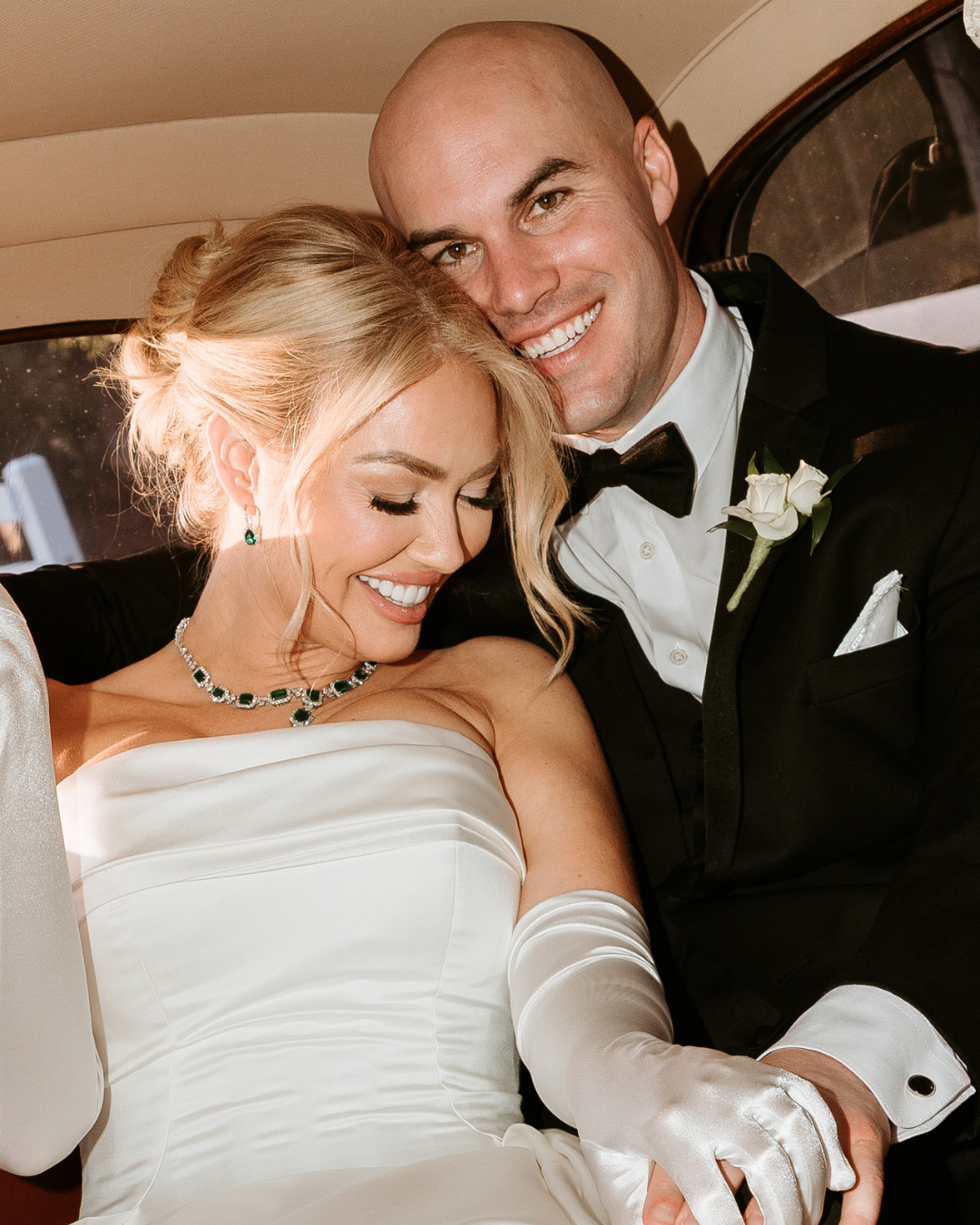 bride and groom in getaway car smiling, bride has white sik gloves and a strapless dress