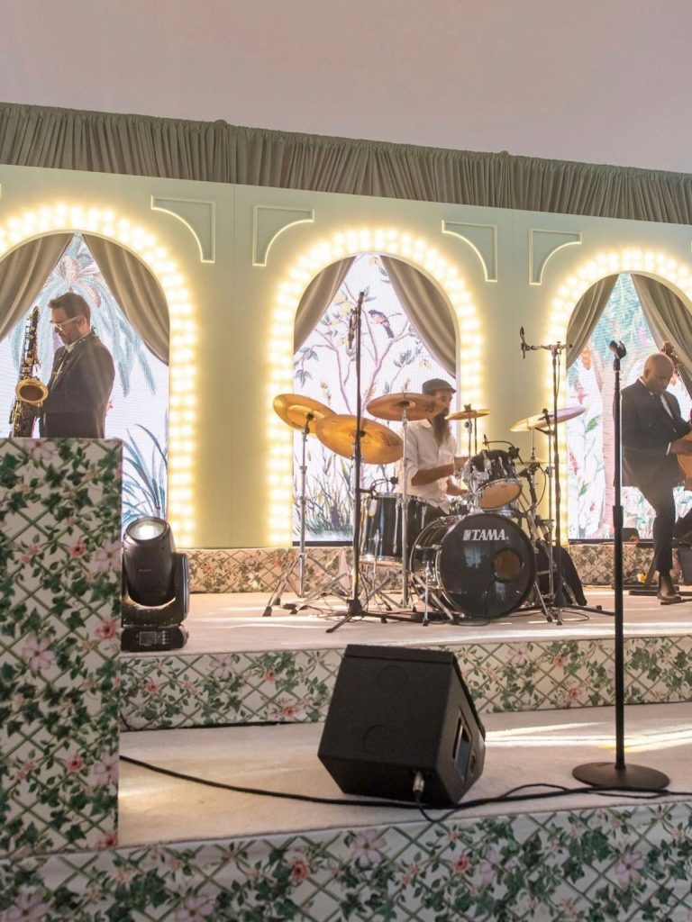 Live wedding band performs on stage with illuminated marquee letters and floral backdrop in elegant ballroom