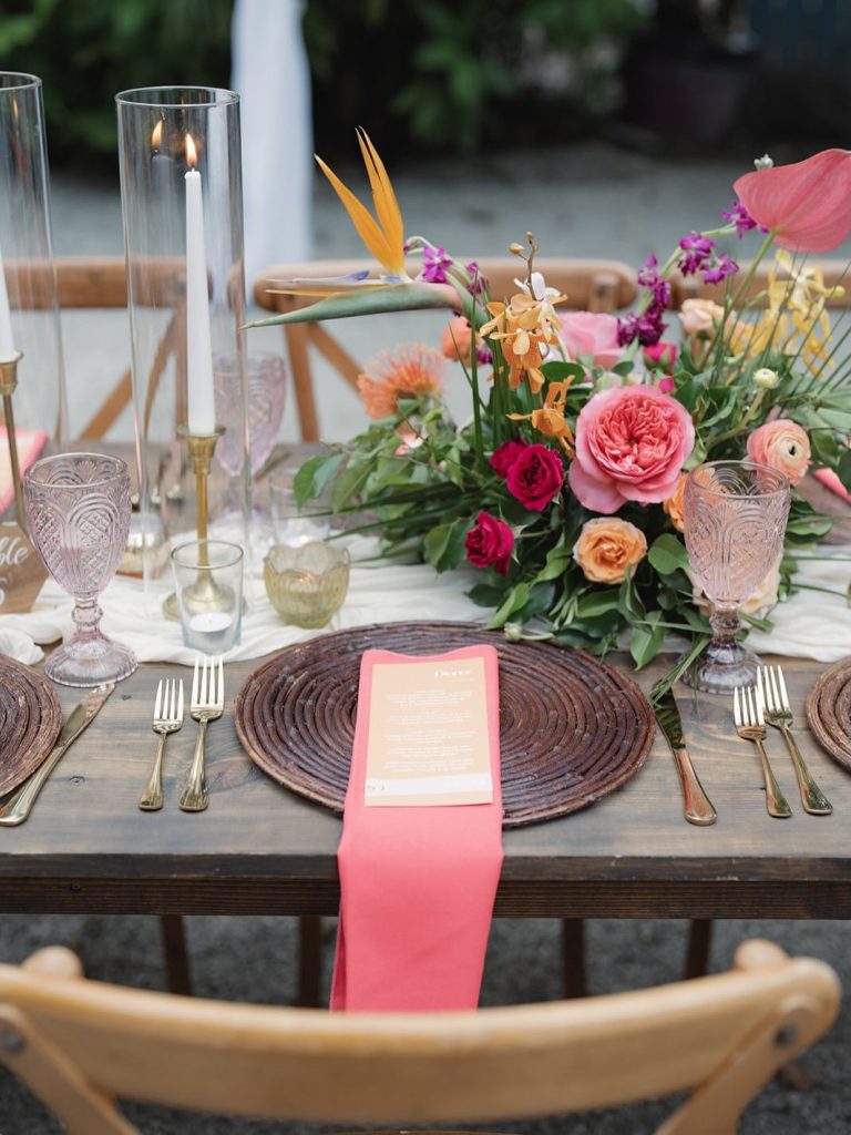 Tropical table setting with vibrant blooms, bird of paradise, coral napkin, and vintage glassware