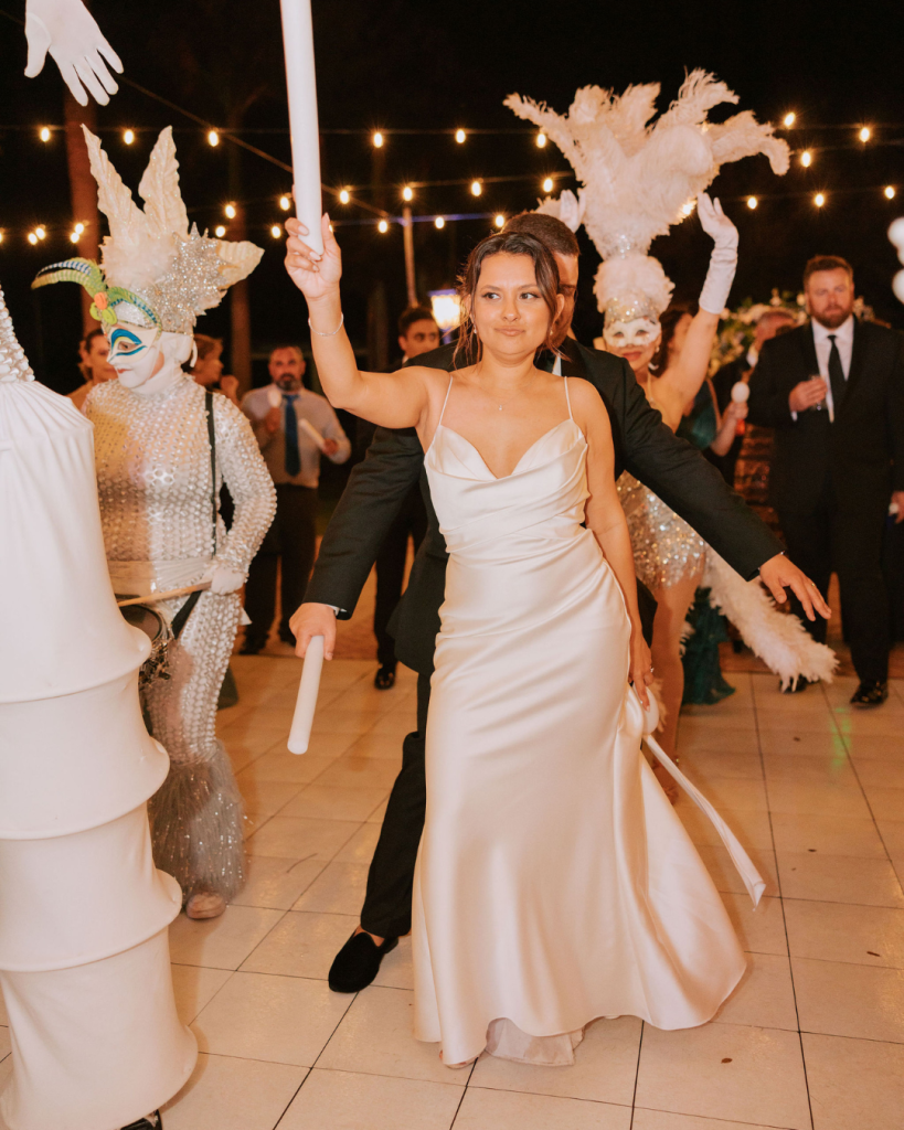 Bride leads festive second line parade with costumed performers and feathered plumes under bistro lights