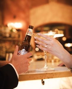 Newlyweds toast with beer bottle and champagne flute, engagement ring visible on bride's hand